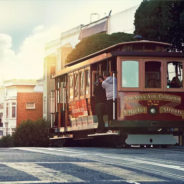 A cable car rounds a hill in San Francisco with passengers looking out the window.